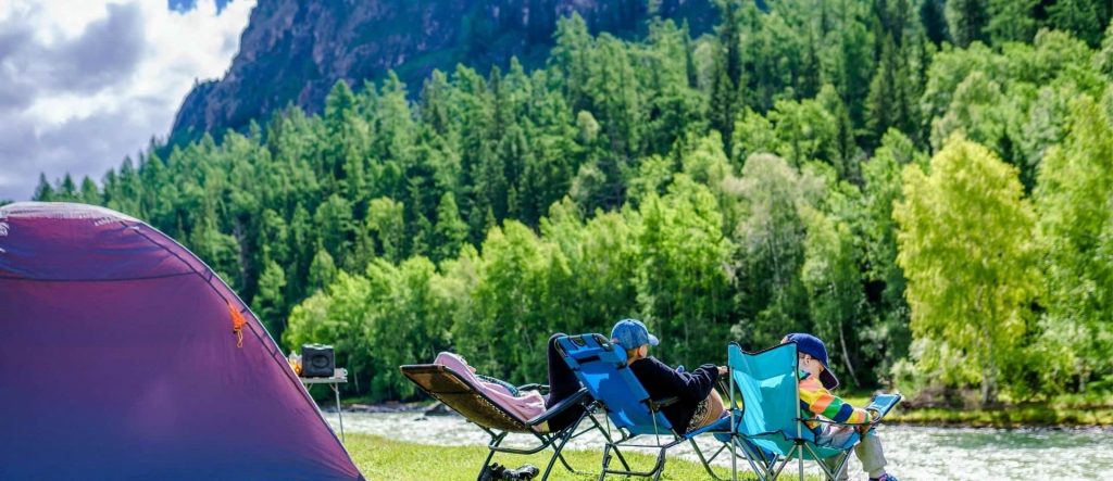 Famille assise à l'extérieur de la tente par rivière et forêt en Suède