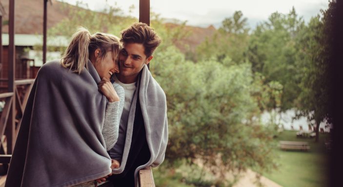 Holiday couple in hotel balcony wrapped in blanket