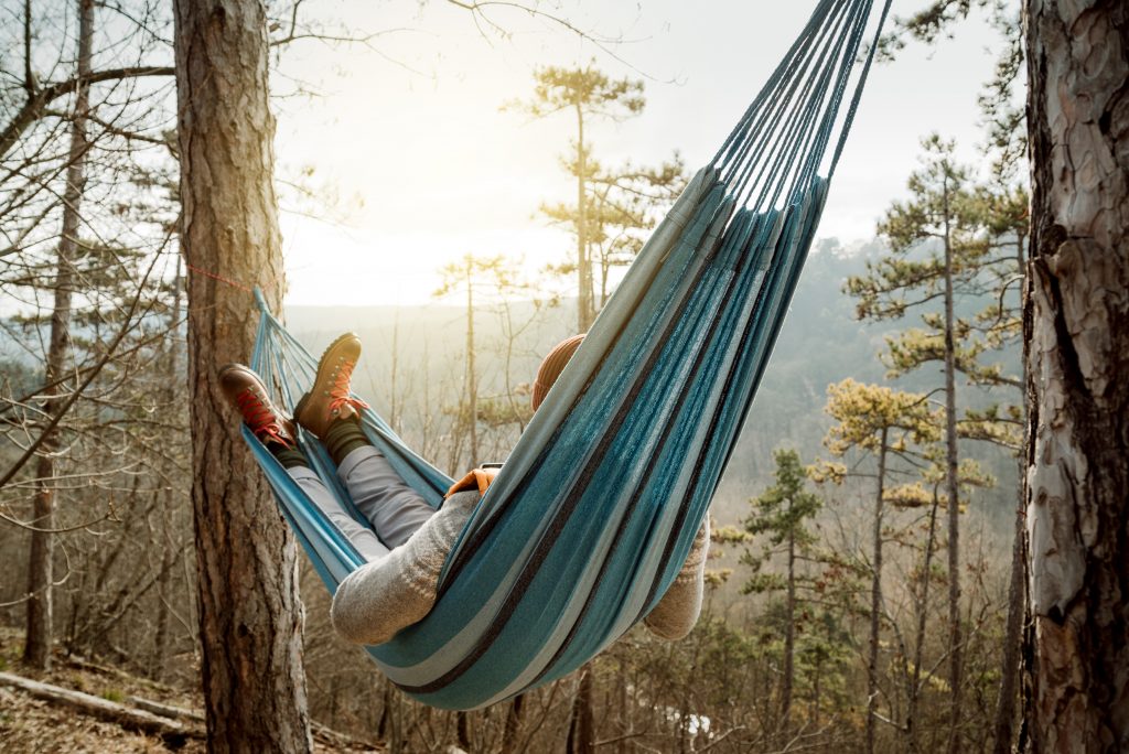 Young happy man relaxing lying in hammock on top of mountain.