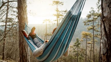 Young happy man relaxing lying in hammock on top of mountain.