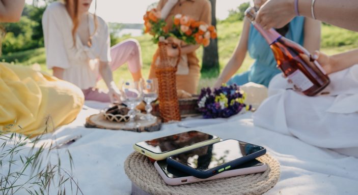 Digital Detox, time for disconnecting from electronic devices. Mobile phones on basket on picnic background. Group of young woman hanging out together on a picnic in nature at no phone zone