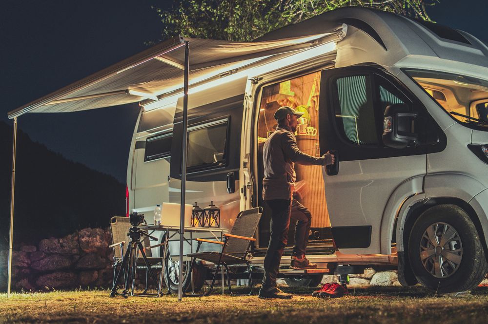 Man at campervan in campsite at night | Homme à un camping-car dans un camping la nuit