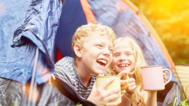 Deux enfants rigolent dans une tente en camping.