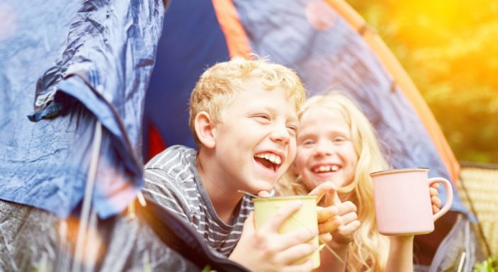 Deux enfants rigolent dans une tente en camping.