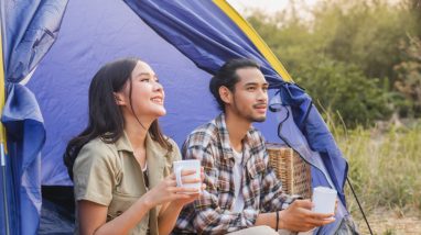 Frau und Mann sitzen nebeneinander in einem Zelt, trinken aus Tassen, schauen glücklich nach draußen.