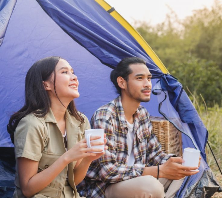 Frau und Mann sitzen nebeneinander in einem Zelt, trinken aus Tassen, schauen glücklich nach draußen.