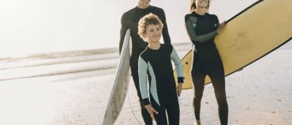 Smiling family walking along the beach with surfboards in spring