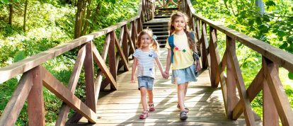 Des sœurs marchant sur un pont en bois à travers une forêt jusqu'à un camping écologique.