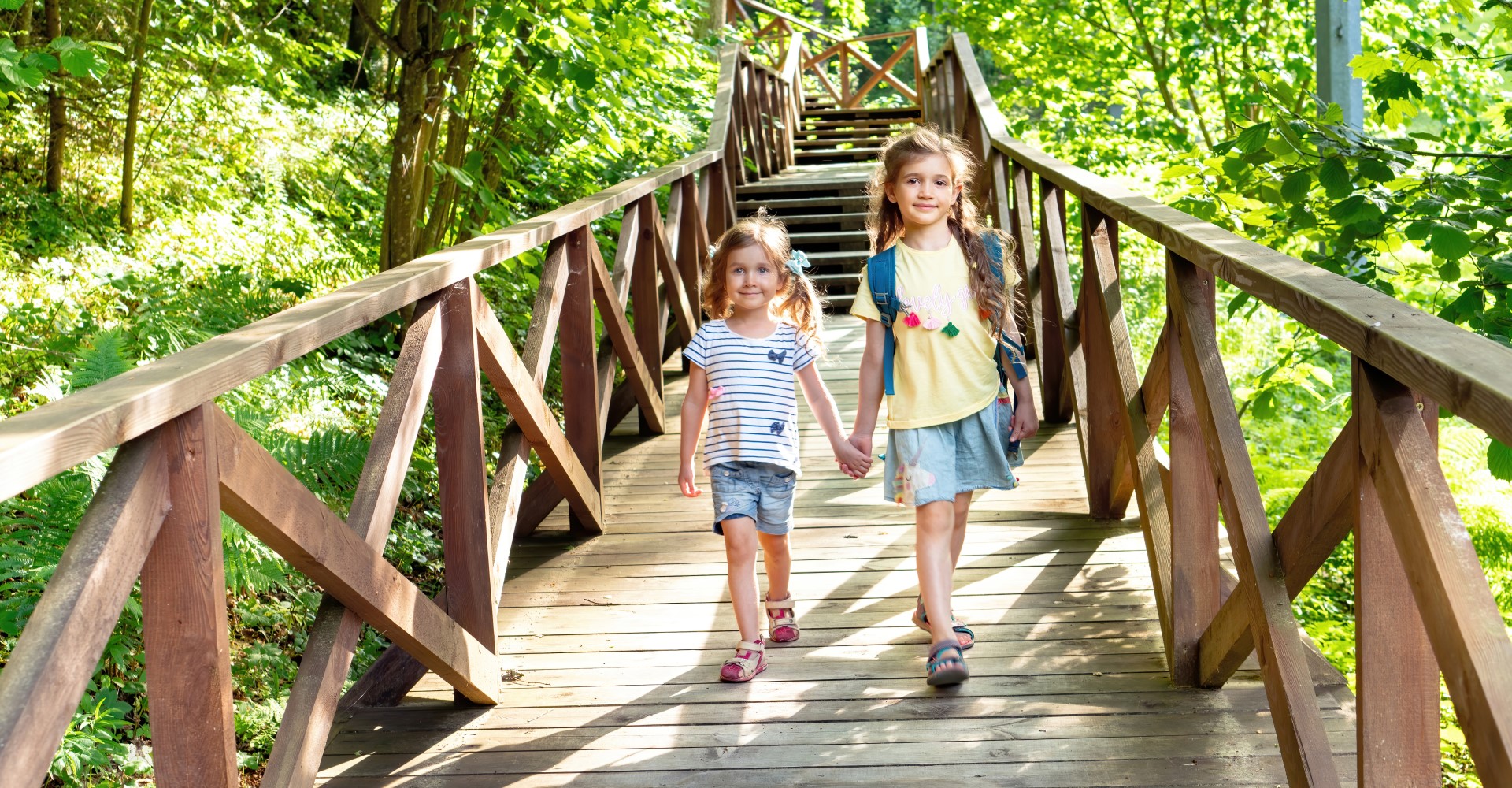 sisters walking on a wooden bridge through forest to an eco-friendly campsite