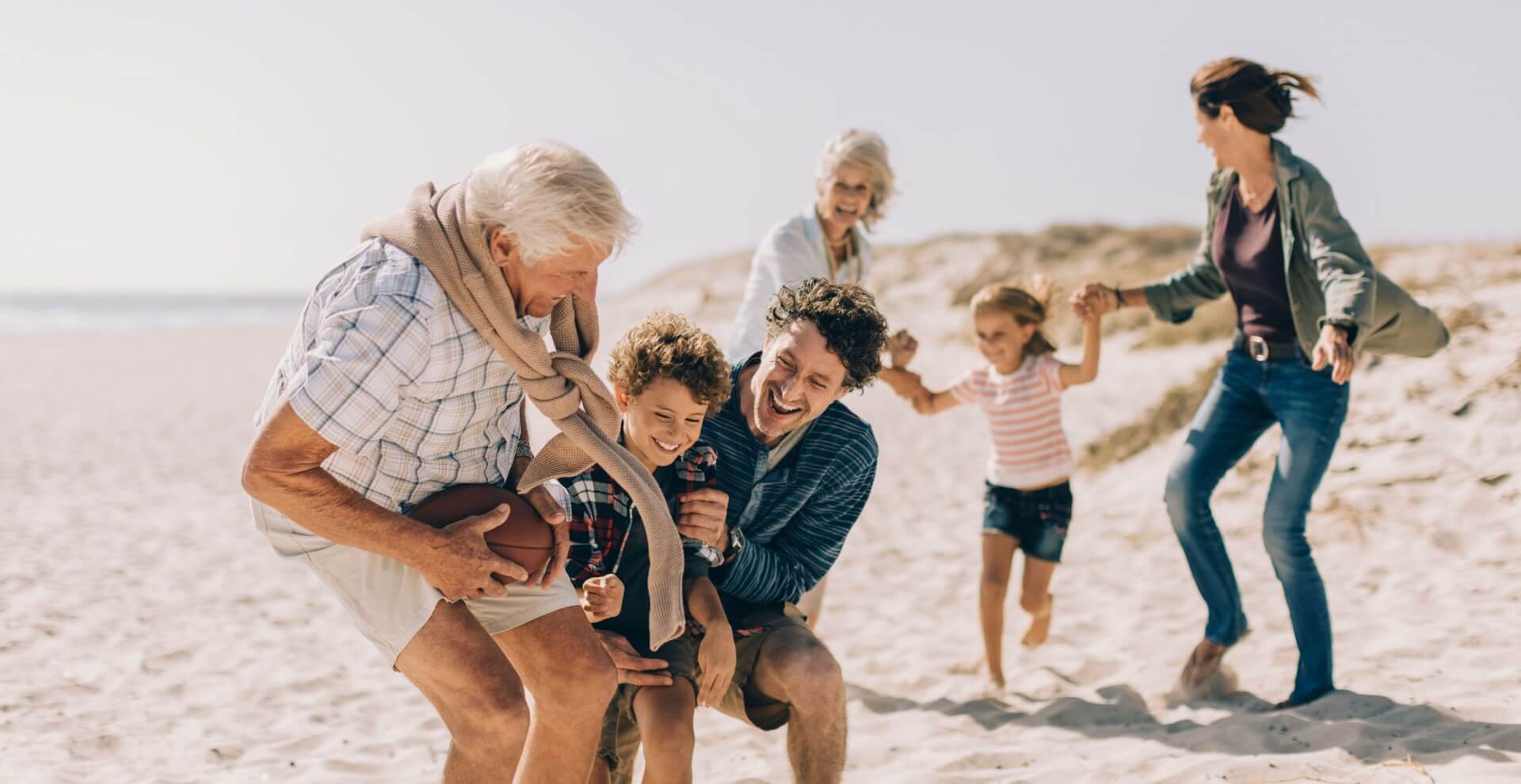 Three generation family playing on a sunny beach in autumn