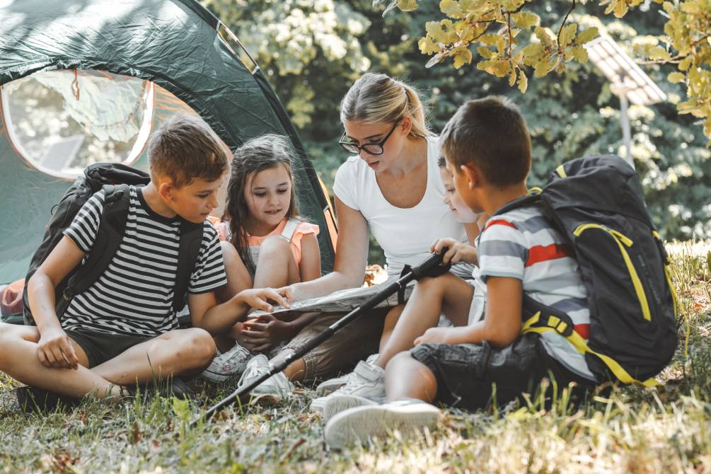 An adult and three kids planning activities at a campsite | Un adulto e tre bambini pianificano le attività in un campeggio