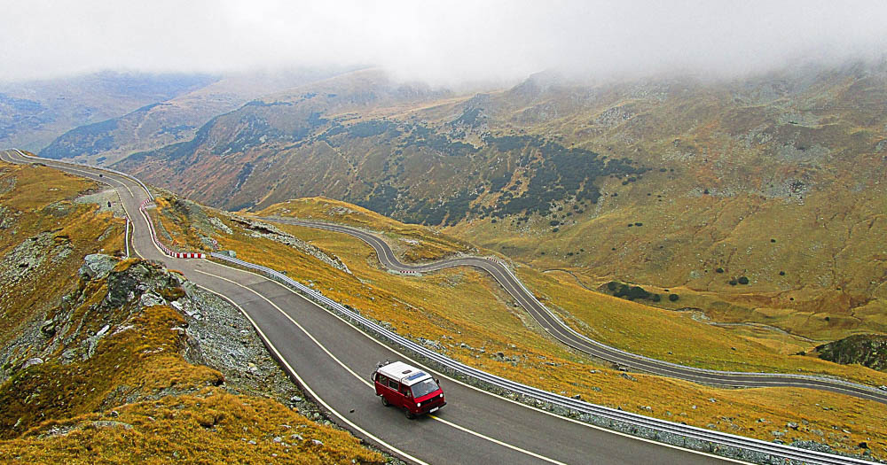 camper rosso viaggia su strada tra le montagne