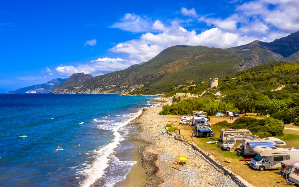Campingplatz auf Korsika mit Wohnmobilen mit Blick auf das Meer und Berge im Hintergrund