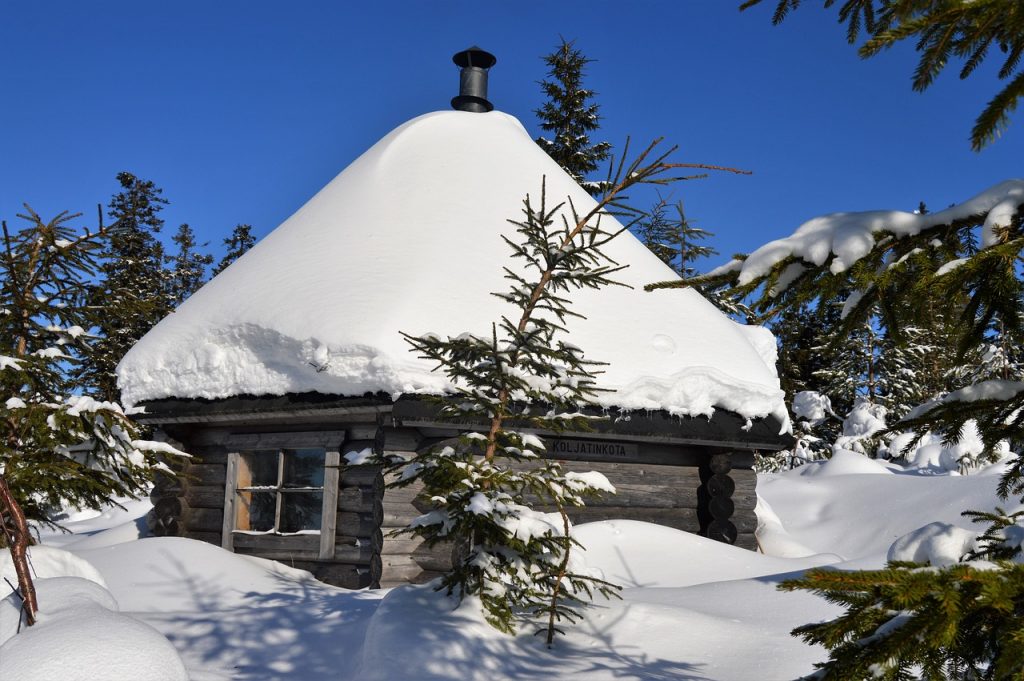 Gemütliche Hütte in Waldlandschaft vor blauem Himmel, mit Schnee bedeckt - Wintercamping, Urlaub im Schnee