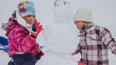 Zwei Kinder in Schneeanzügen bauen einen Schneemann, Wintercamping