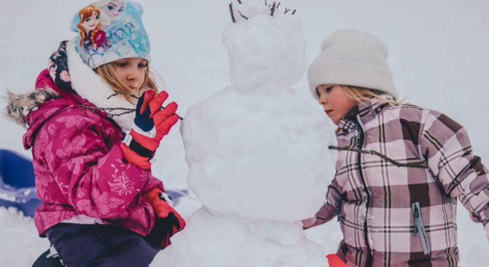 Zwei Kinder in Schneeanzügen bauen einen Schneemann, Wintercamping