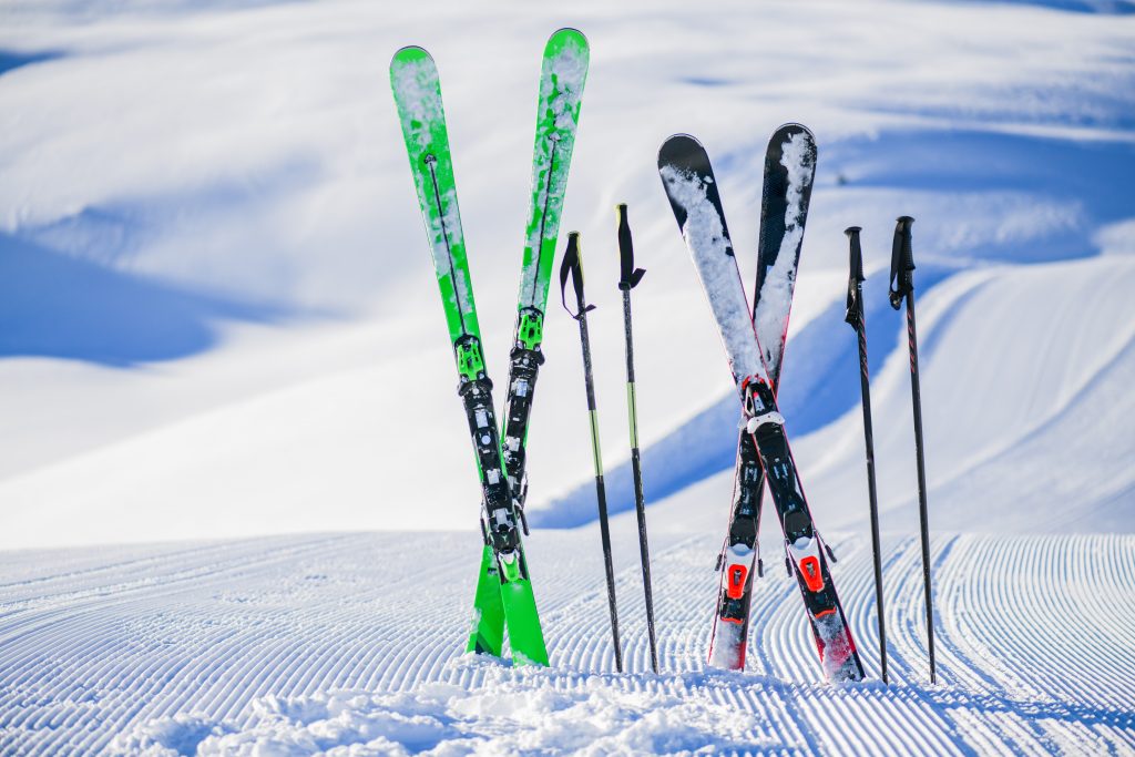 Zwei Paar Skier und Stöcke stecken auf einer Piste im Schnee, Wintercamping, Urlaub im Schnee