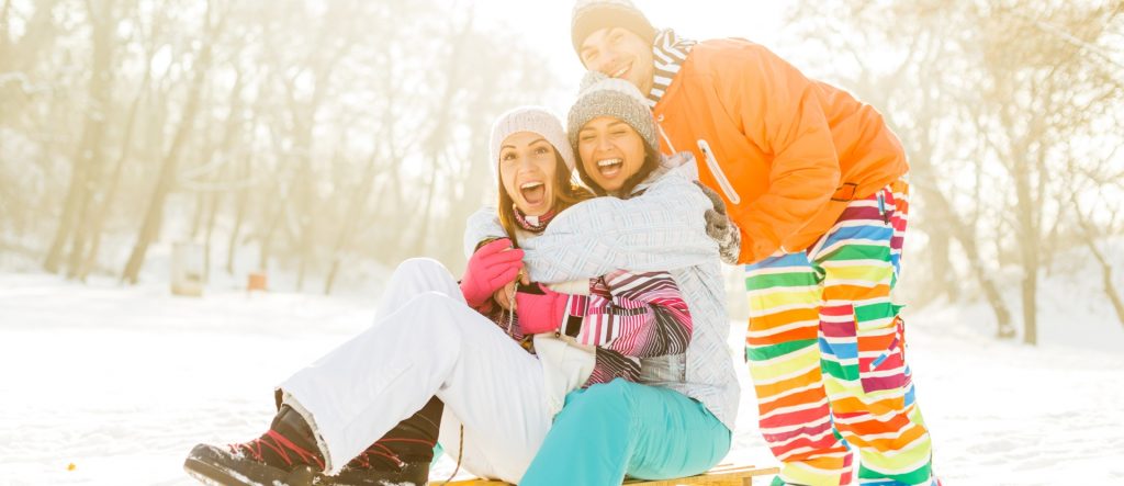 Drei Freunde sind in Schneeanzüge gepackt und schauen lachend in die Kamera, Urlaub im Schnee