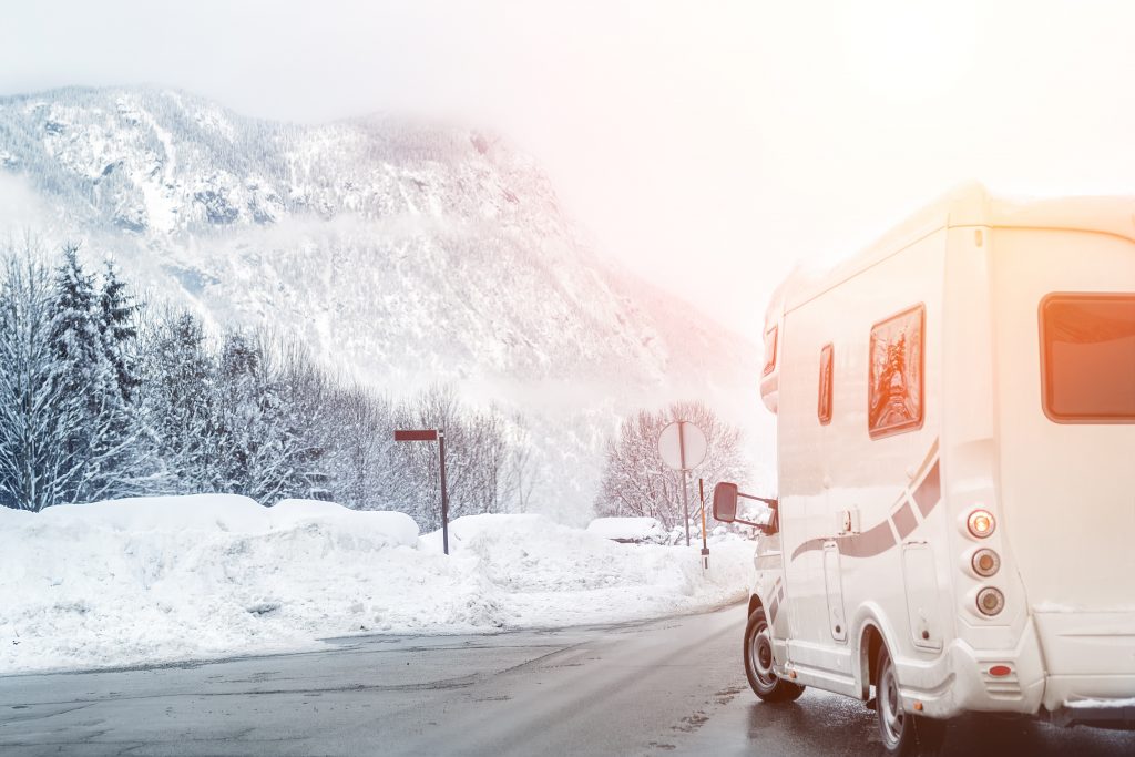 Wohnmobil fährt auf einer Straße in einer winterlichen Landschaft, im Hintergrund Berge