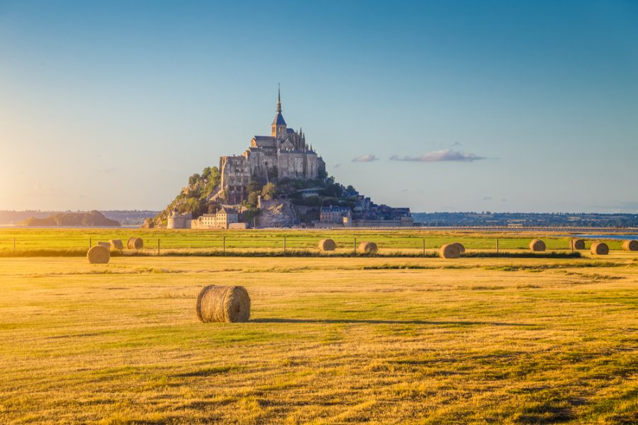 Felder mit Heuballen und im Hintergrund Ausblick auf das historische Mont-Saint-Michel in der Normandie, Frankreich