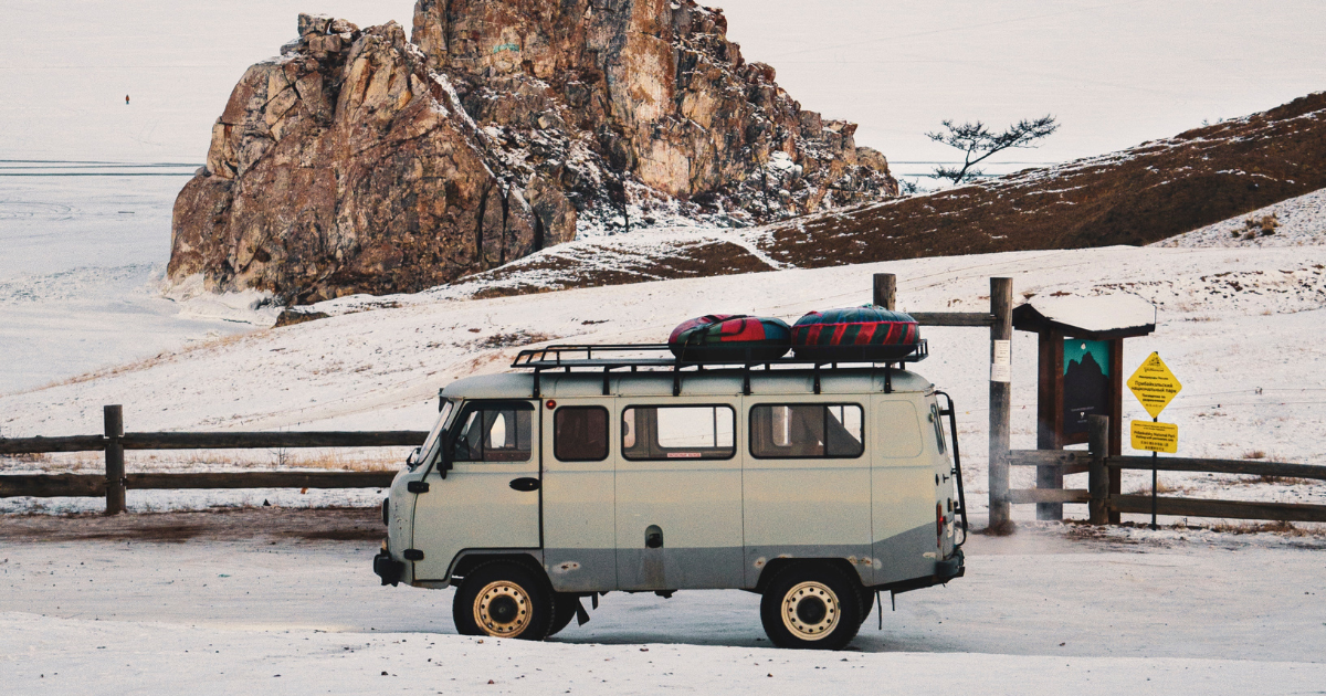 Campervan vor einer winterlichen Landschaft, im Hintergrund Berge