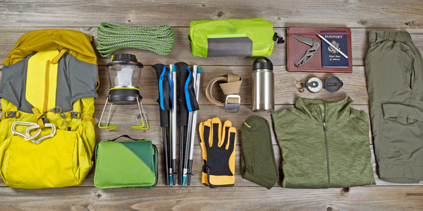 Camping Ausrüstungsgegenstände aufgereiht: Rucksack, Campingkocher, Seil, Stäcke, Handschuhe, Thermosflasche, Socken, Jacke, Hose, Taschenmesser, Kompass usw.