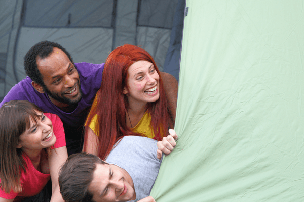 Gruppe von vier Personen schaut lachend aus einem Zelt