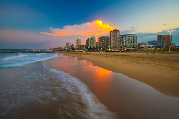 Strand bei Sonnenuntergang, im Hintergrund ragen Gebäude in den Himmel in Durban, KZN, Südafrika