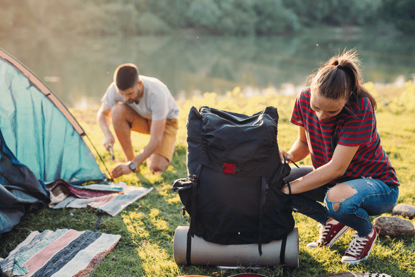 Paar beim Zeltaufbau, Frau entpackt den Rucksack, Mann im Hintergrund am Zelt