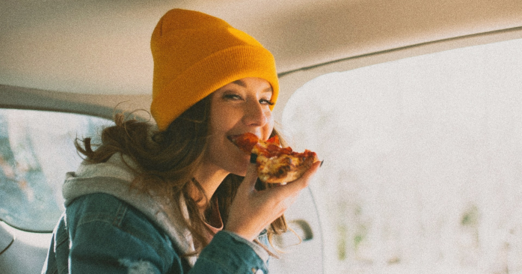 girl in winter clothes eating pizza in the car