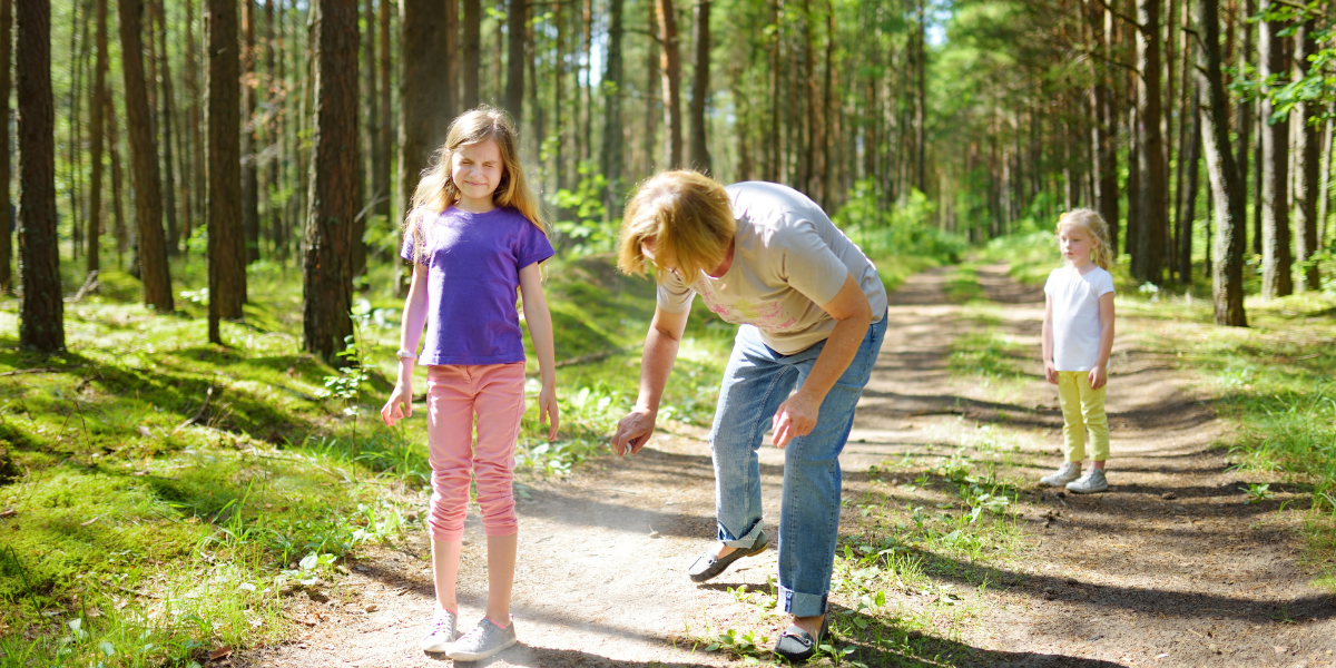 Mutter sprüht Mückenspray auf die Beine ihrer Tochter bei einem Waldspaziergang