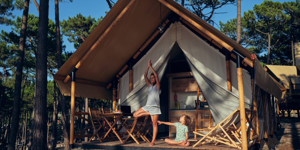 Eco-camping - Mother doing yoga on the terrace of safari-tent hut 