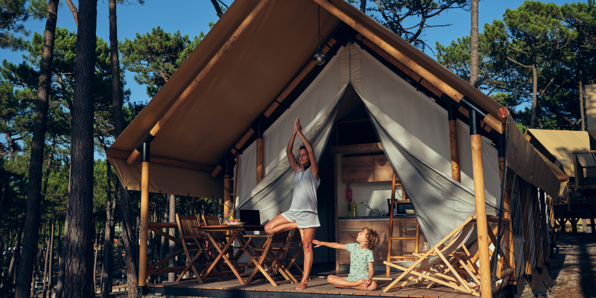 Frau in einer Yogapose, daneben ihr Kind, vor einer Eco Glamping Unterkunft