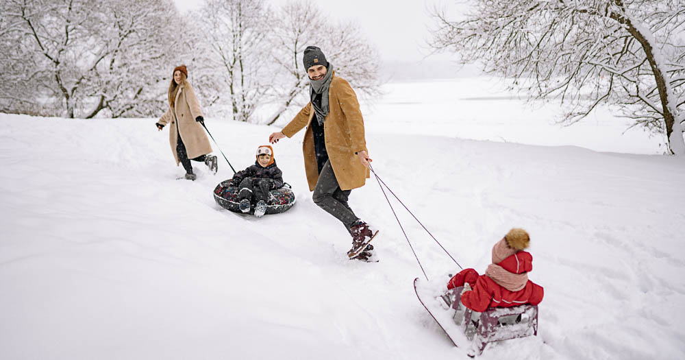 una famiglia con due genitori e due bambini gioca sulla neve con degli slittini