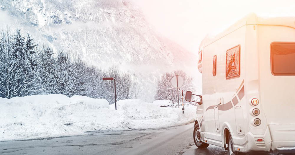 Camper sul lato della strada con paesaggio montano innevato sullo sfondo