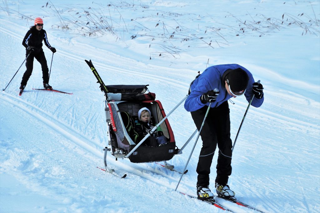 un uomo fa sci di fondo trainando un passeggino attrezzato per la neve con dentro un bimbo piccolo