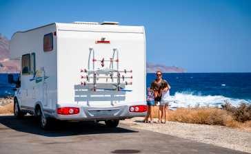 Frau steht neben einem Wohnmobil, im Hintergrund Strand und Meer