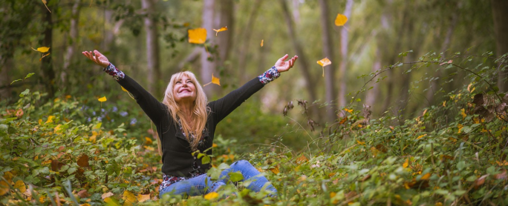 Lächelnde Frau wirft Blätter in die Luft im Wald