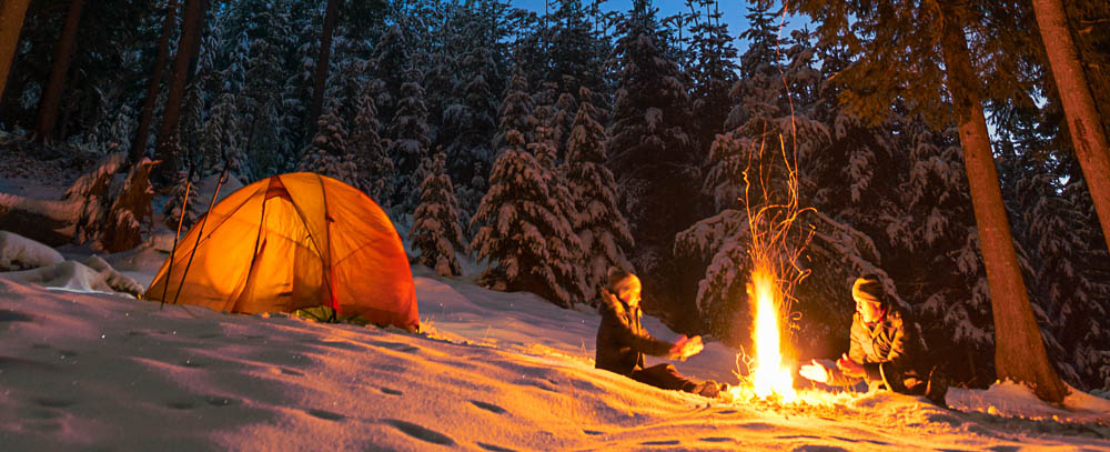 coppia in campeggio in tenda in inverno davanti un falò nella neve
