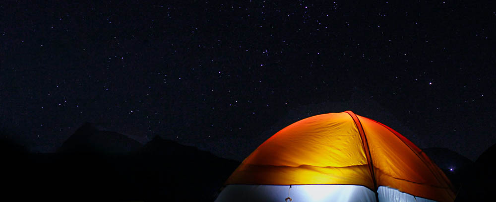 tenda arancione con luce accesa sotto il cielo stellato