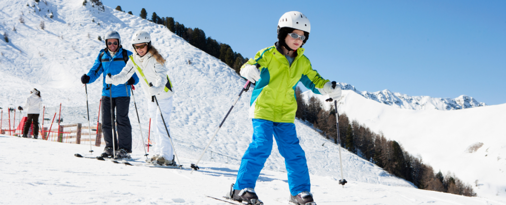 Child learning to ski on fresh snow slopes with parents behind her.