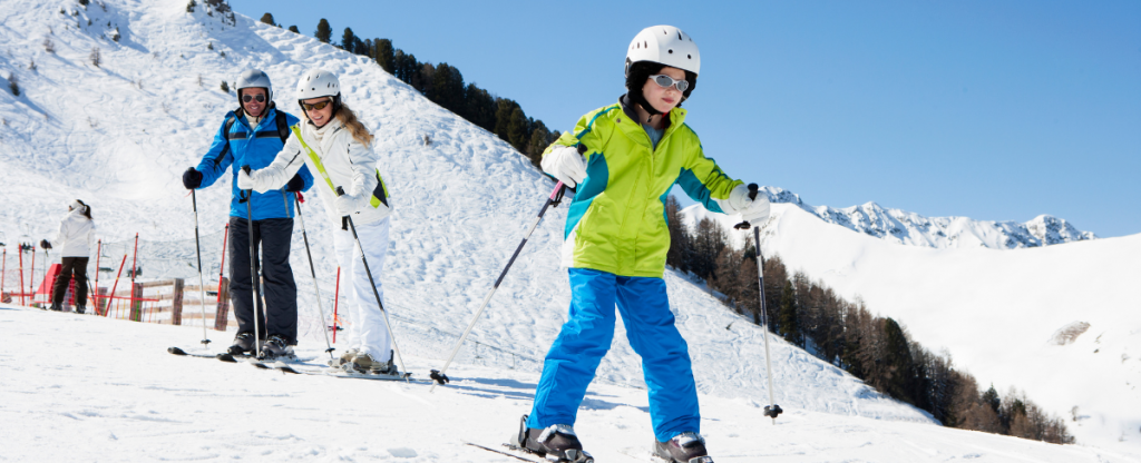 Child learning to ski on fresh snow slopes with parents behind her. 